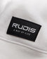 A close-up of a white fabric featuring a black rectangular tag that reads RUDIS A WAY OF LIFE in bold lettering