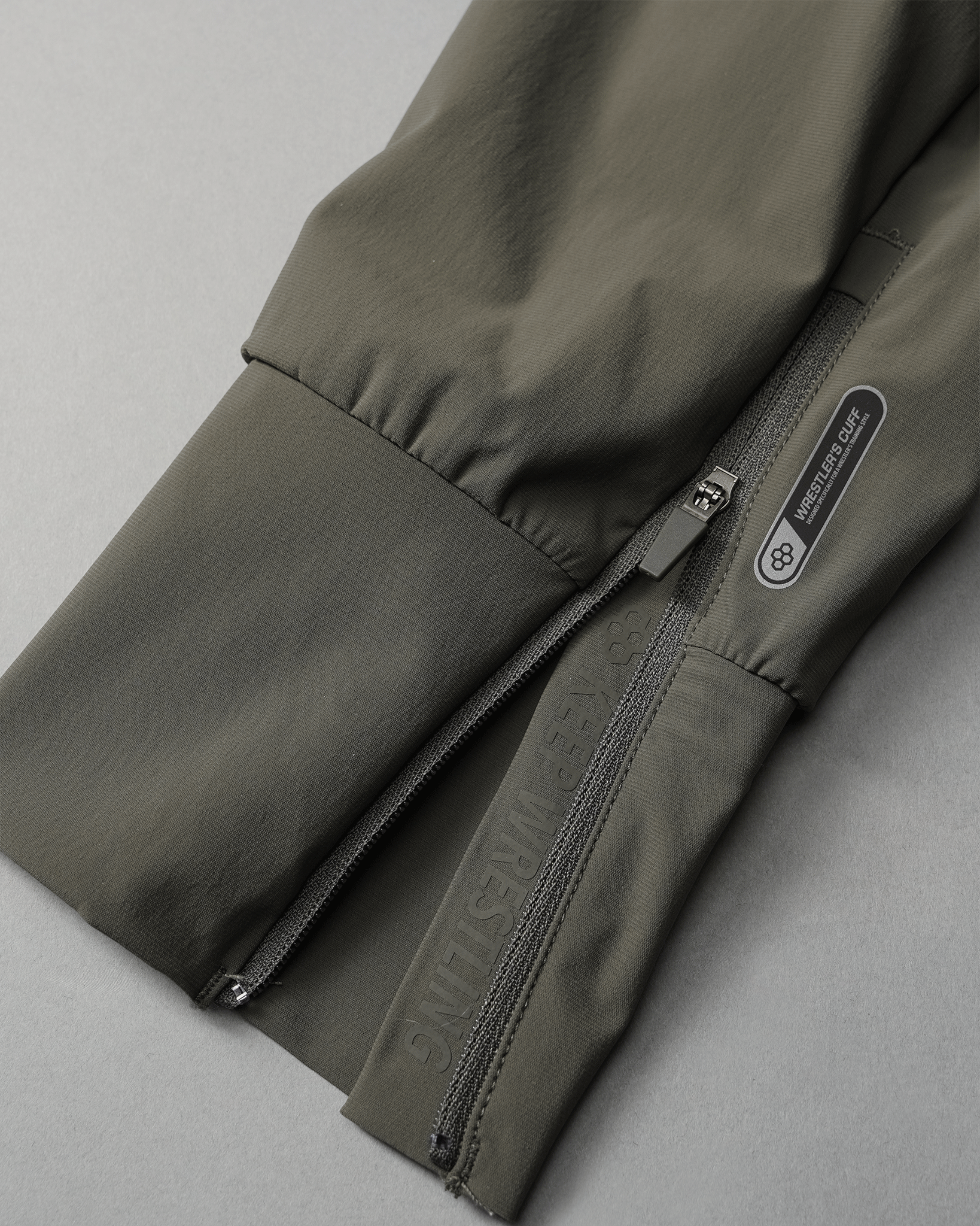 A dark green sleeve features a zipper and printed text 'KEEP WRESTLING,' set against a soft gray background.