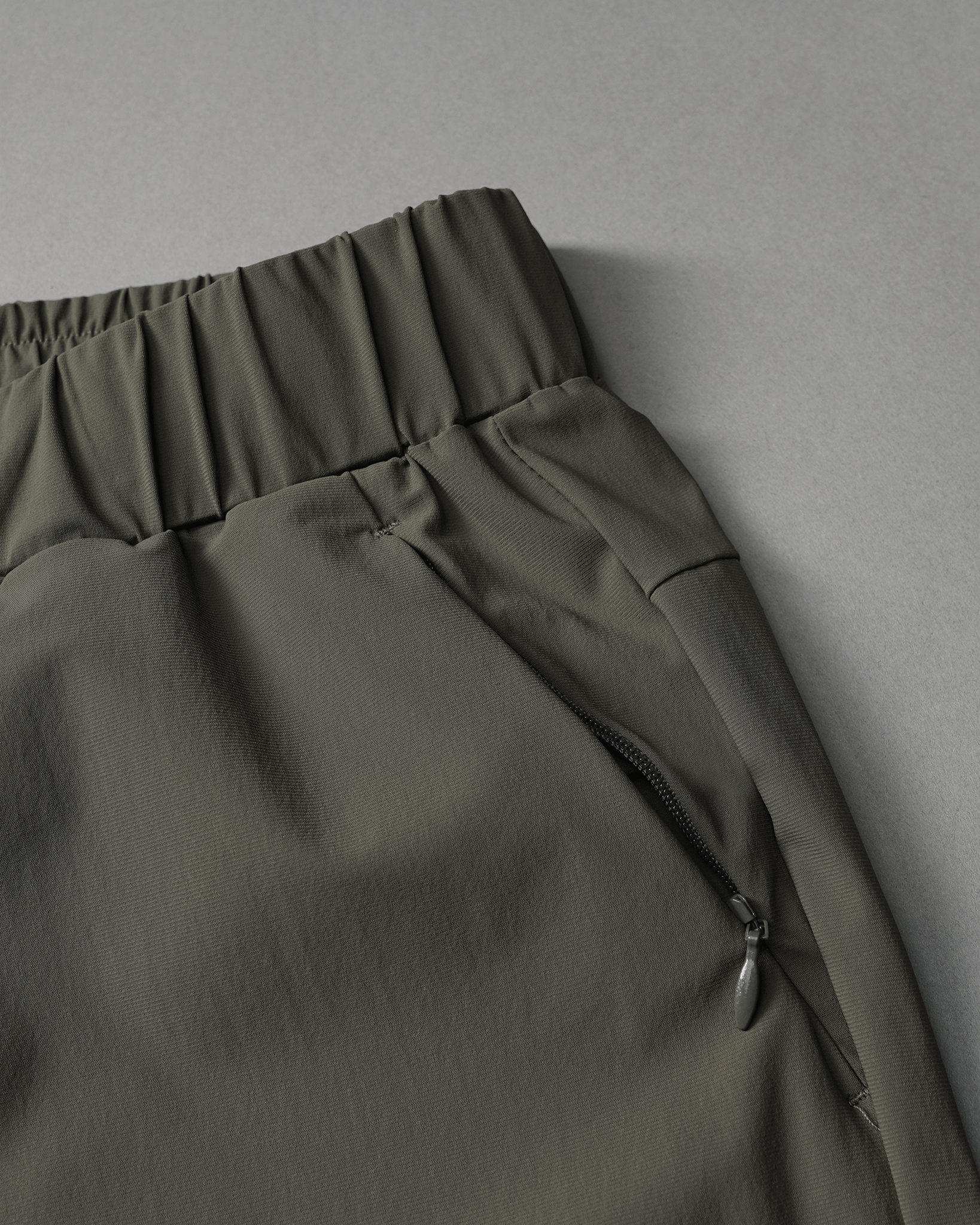 A close-up of pants with a soft elastic waistband and a zipper pocket, showcased against a muted gray background.