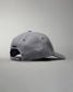 A gray baseball cap with a curved brim and adjustable strap at the back, equipped with ventilation eyelets and an embroidered logo, set against a soft gray background.