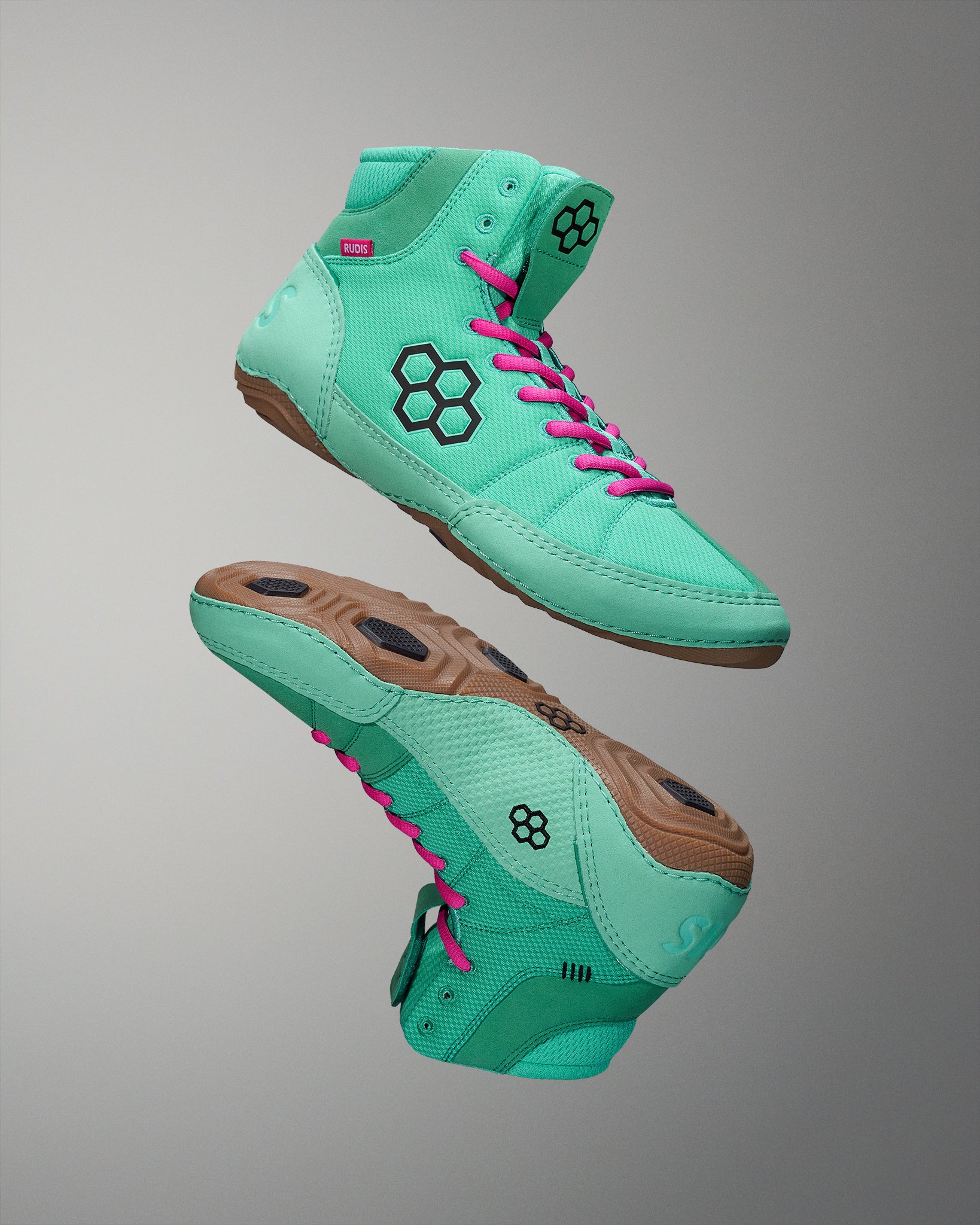 High-top athletic shoes showcase a mint green upper with pink laces and brown rubber soles, featuring a black hexagon logo and textured elements for traction, presented against a minimalist background.