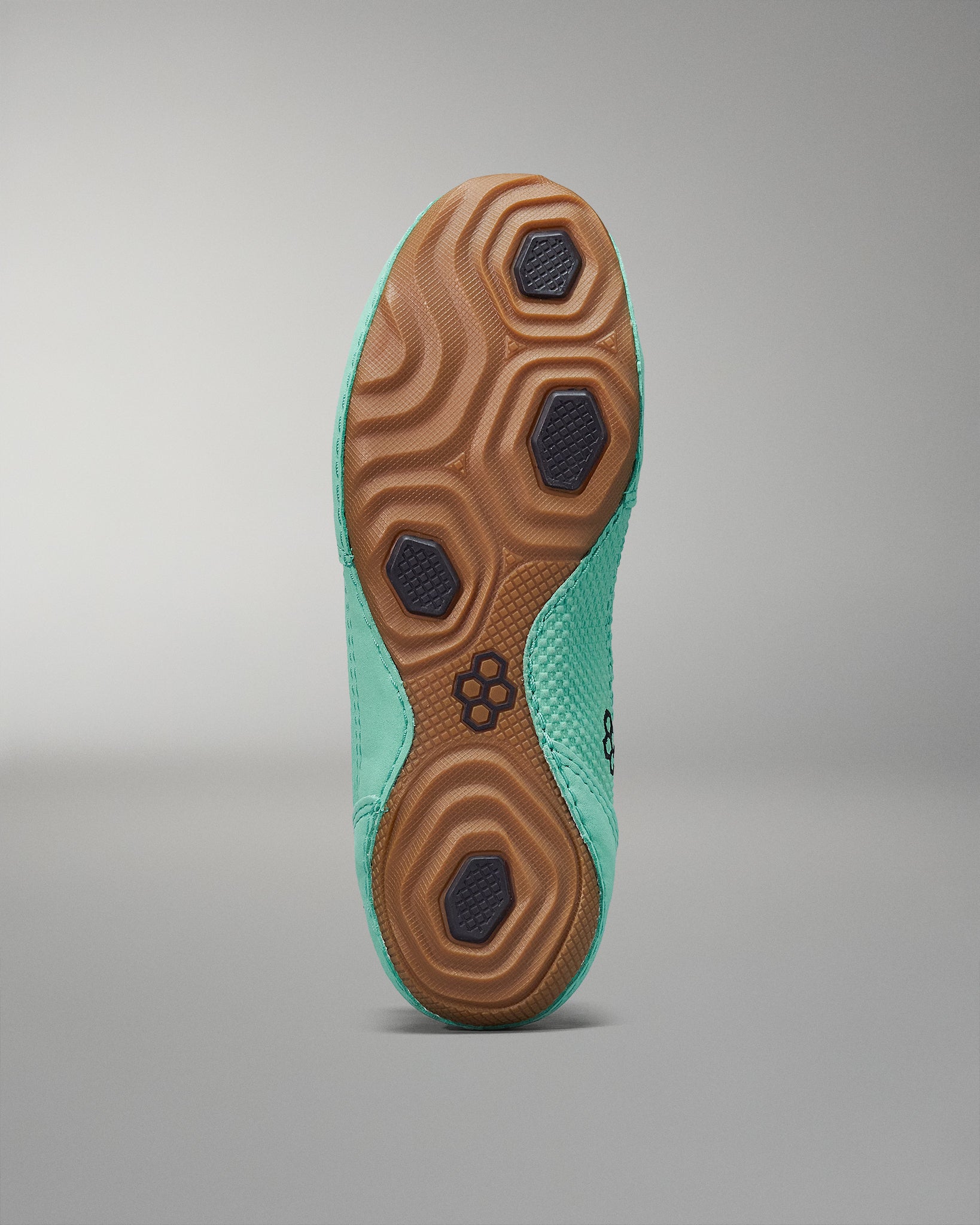 The sole of a shoe combines a vibrant turquoise upper with textured patterns and brown rubber sections for improved grip against a soft gray background.