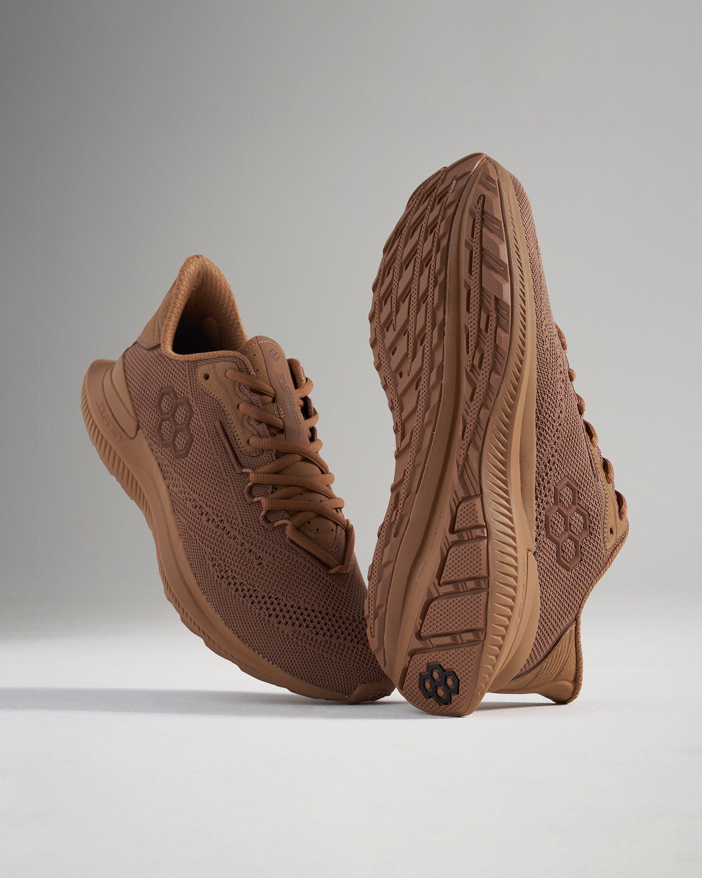 A pair of sleek brown athletic shoes with a lightweight mesh upper and textured soles positioned to highlight their modern design and performance features