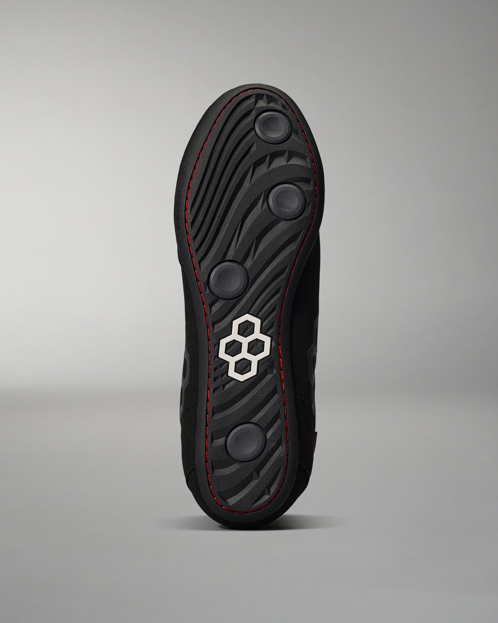 The underside of a shoe showcases a textured black sole with circular grip pads and a prominent logo against a neutral gray background.