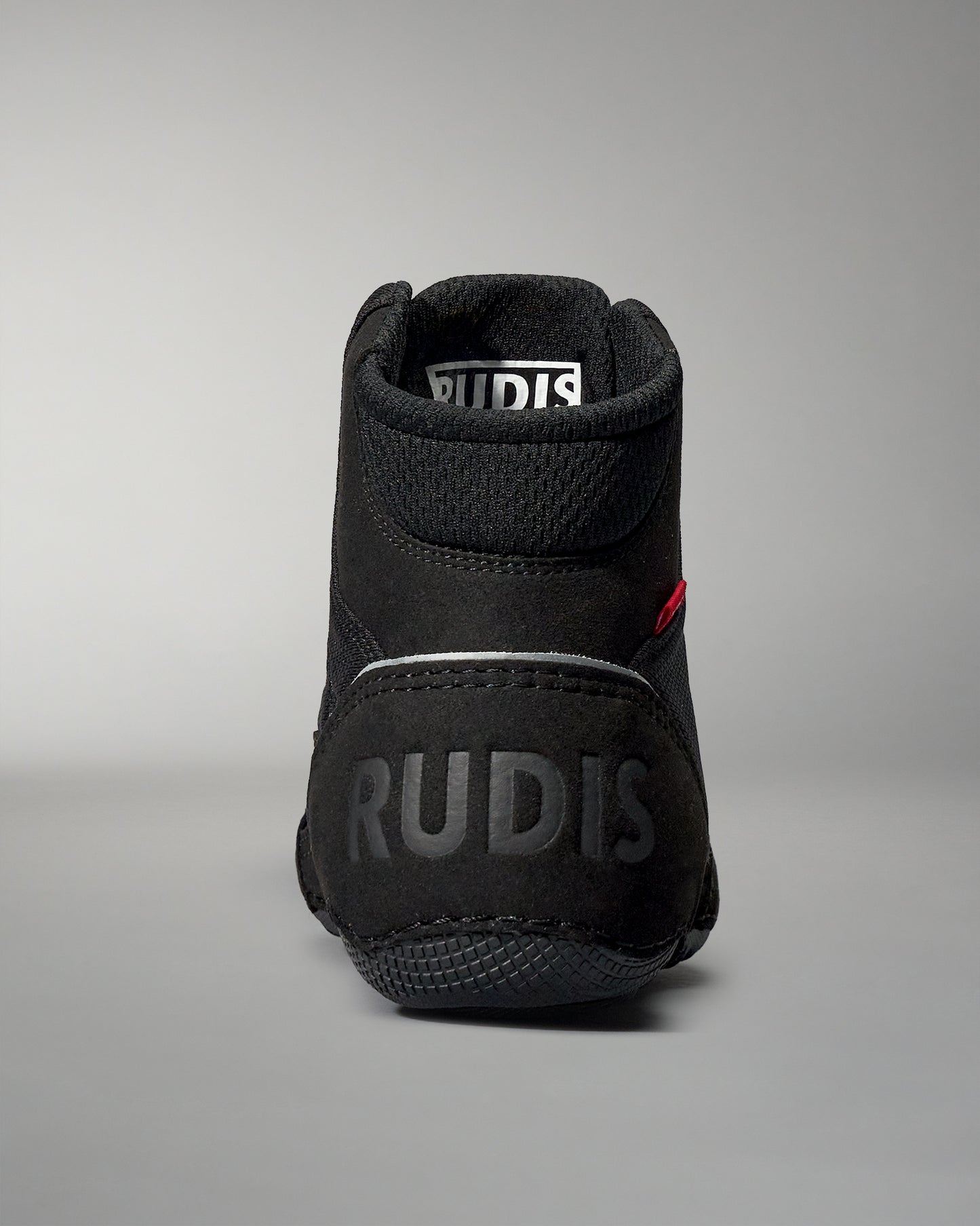 A high-top black athletic shoe with a padded collar and textured surface, featuring an embossed 'RUDIS' logo on the back, set against a soft gray background.