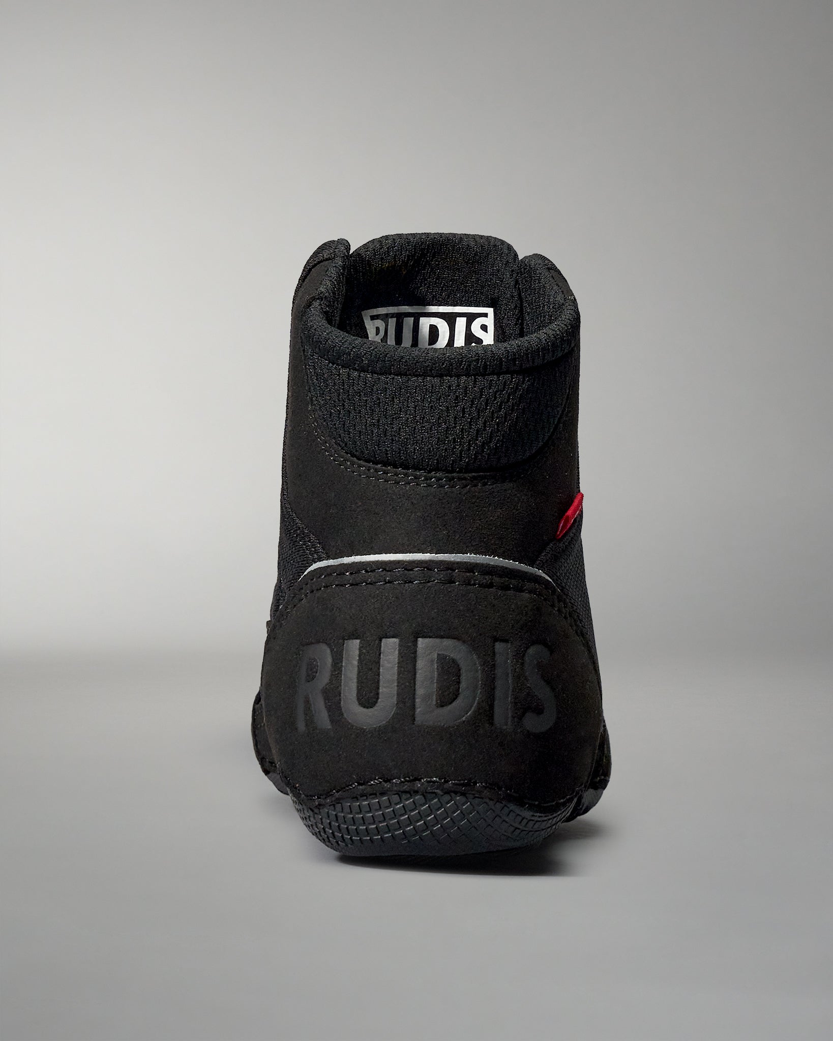 A high-top black athletic shoe with a padded collar and textured surface, featuring an embossed 'RUDIS' logo on the back, set against a soft gray background.