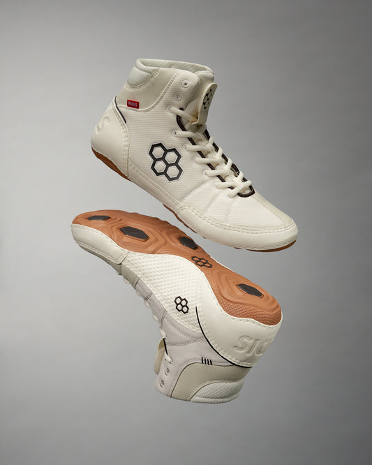 High-top athletic shoe in cream with a textured upper and unique honeycomb-patterned sole against a light gray background, designed for both style and performance.