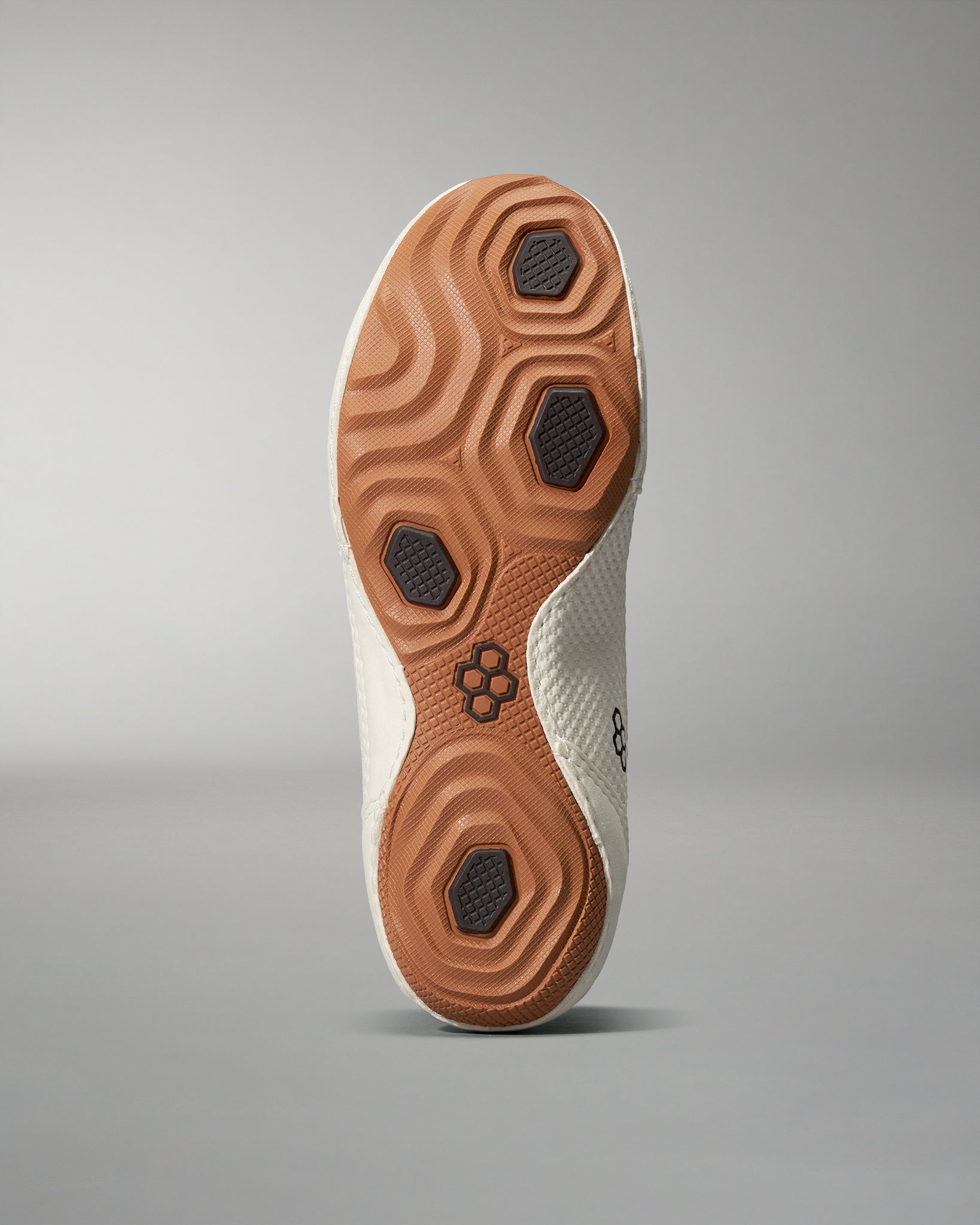 Shoe sole with a textured design of light and dark rubber elements, featuring hexagonal traction points for enhanced grip against a neutral gray background.