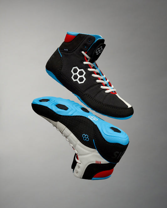 High-top athletic shoes, one black with blue and white accents and the other white with red and black details, featuring textured soles for enhanced grip against a soft gray background.