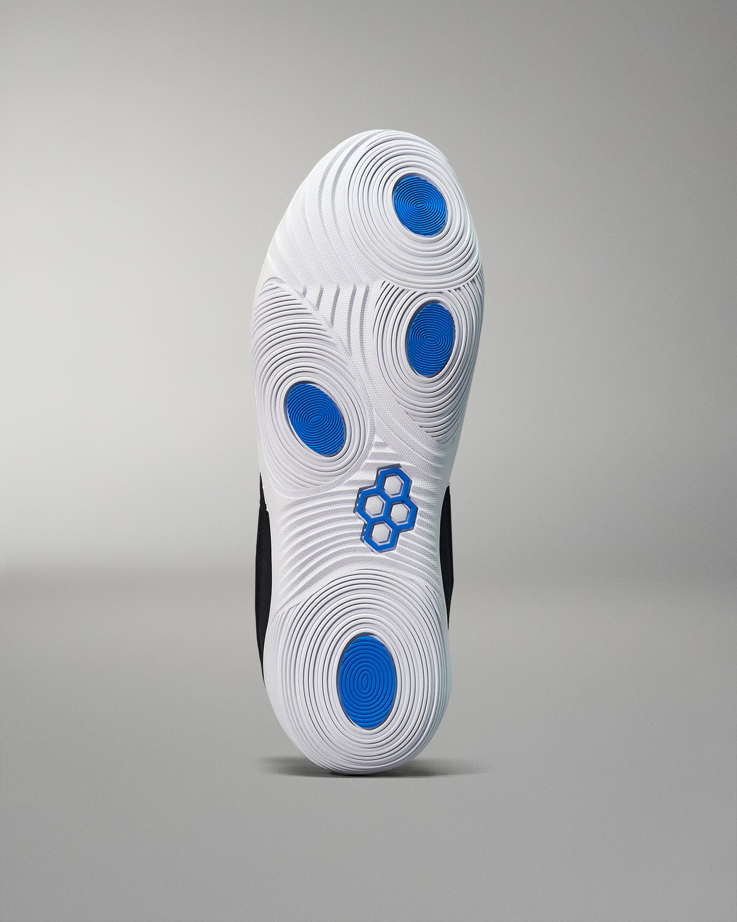 The outsole of a shoe features a white surface with textured patterns and blue circular accents, designed for enhanced traction against a muted gray background.