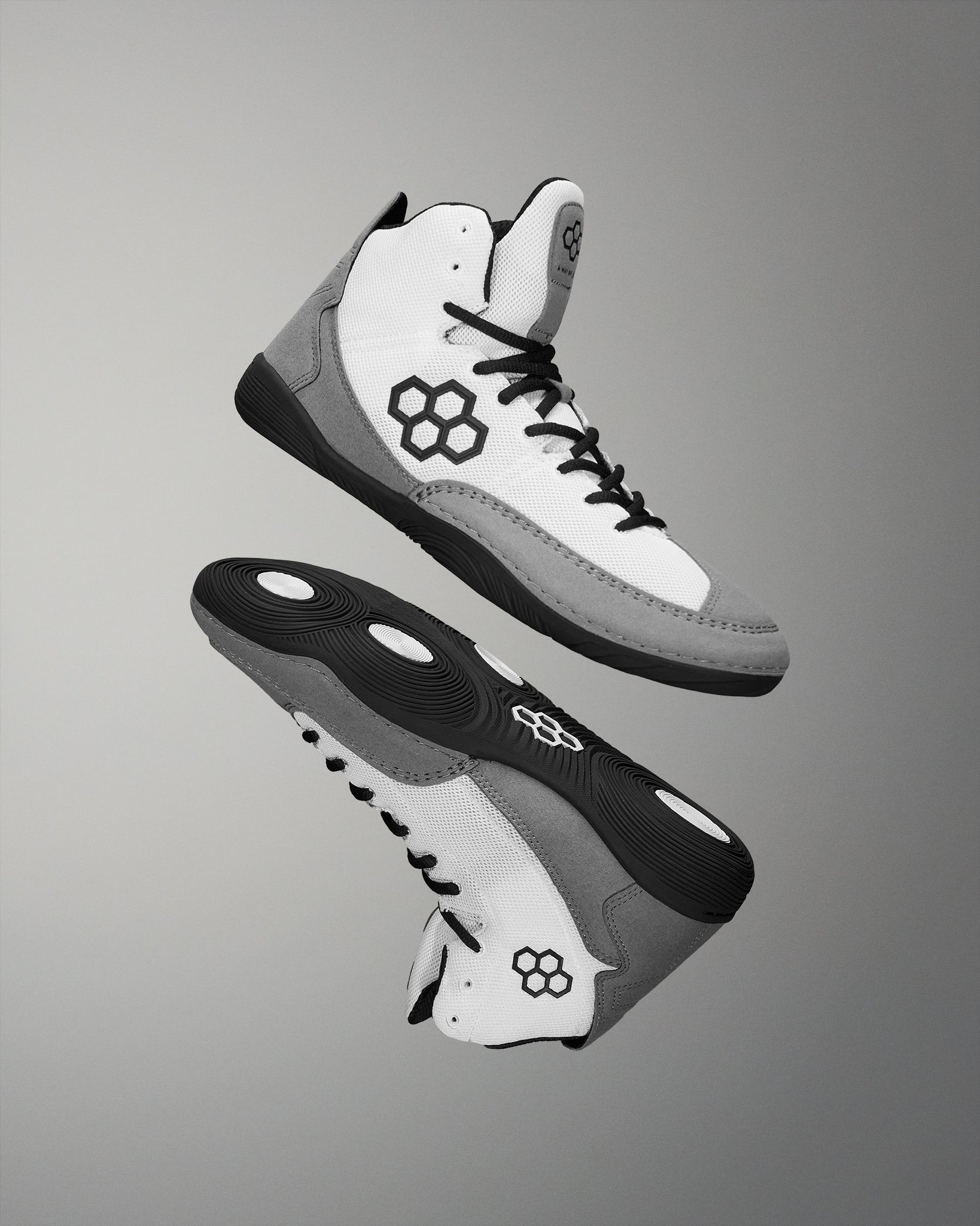 These high-top athletic shoes combine a white mesh upper and grey suede accents, featuring a honeycomb logo and black laces against a neutral background.