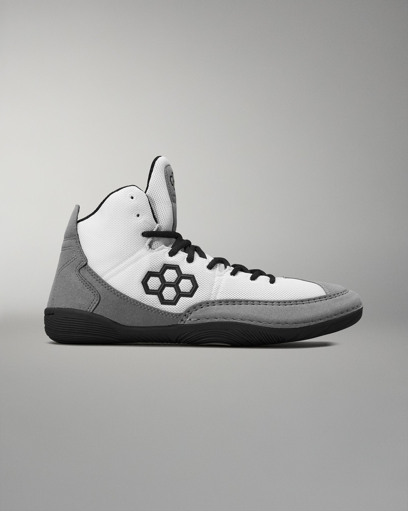 A high-top athletic shoe features a white mesh upper with gray suede accents and a black hexagonal logo, designed for both style and performance.