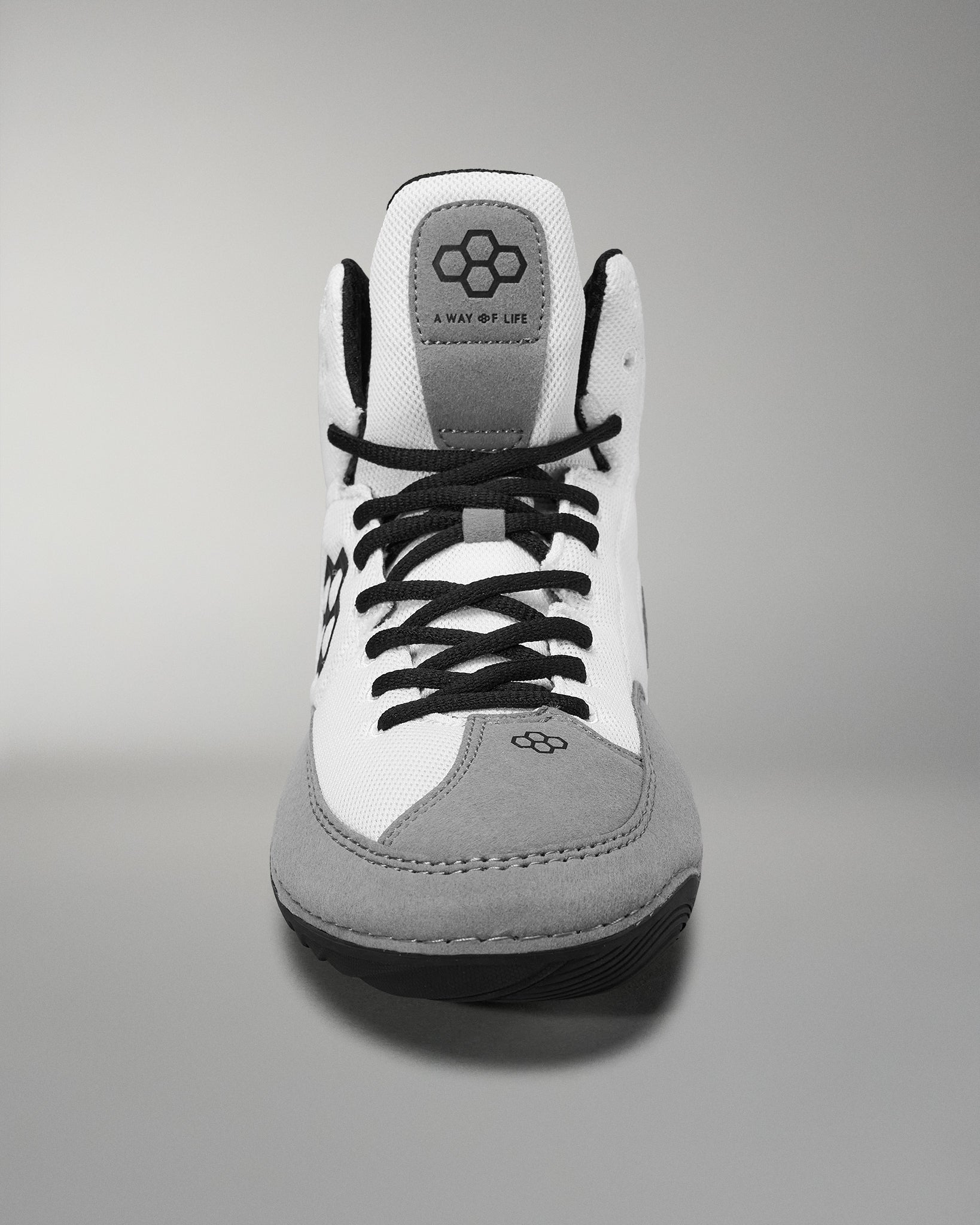 A front view of a black and white sneaker with gray suede details features a logo on the tongue, showcasing a modern style suitable for casual or athletic wear.