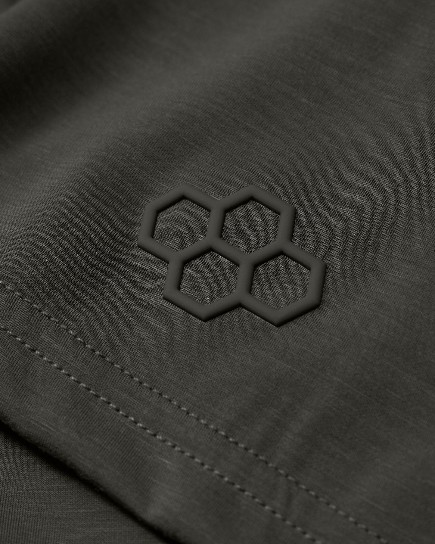 An olive green fabric with a textured hexagonal logo in the corner highlights a modern, minimalist aesthetic, complemented by neat stitching.