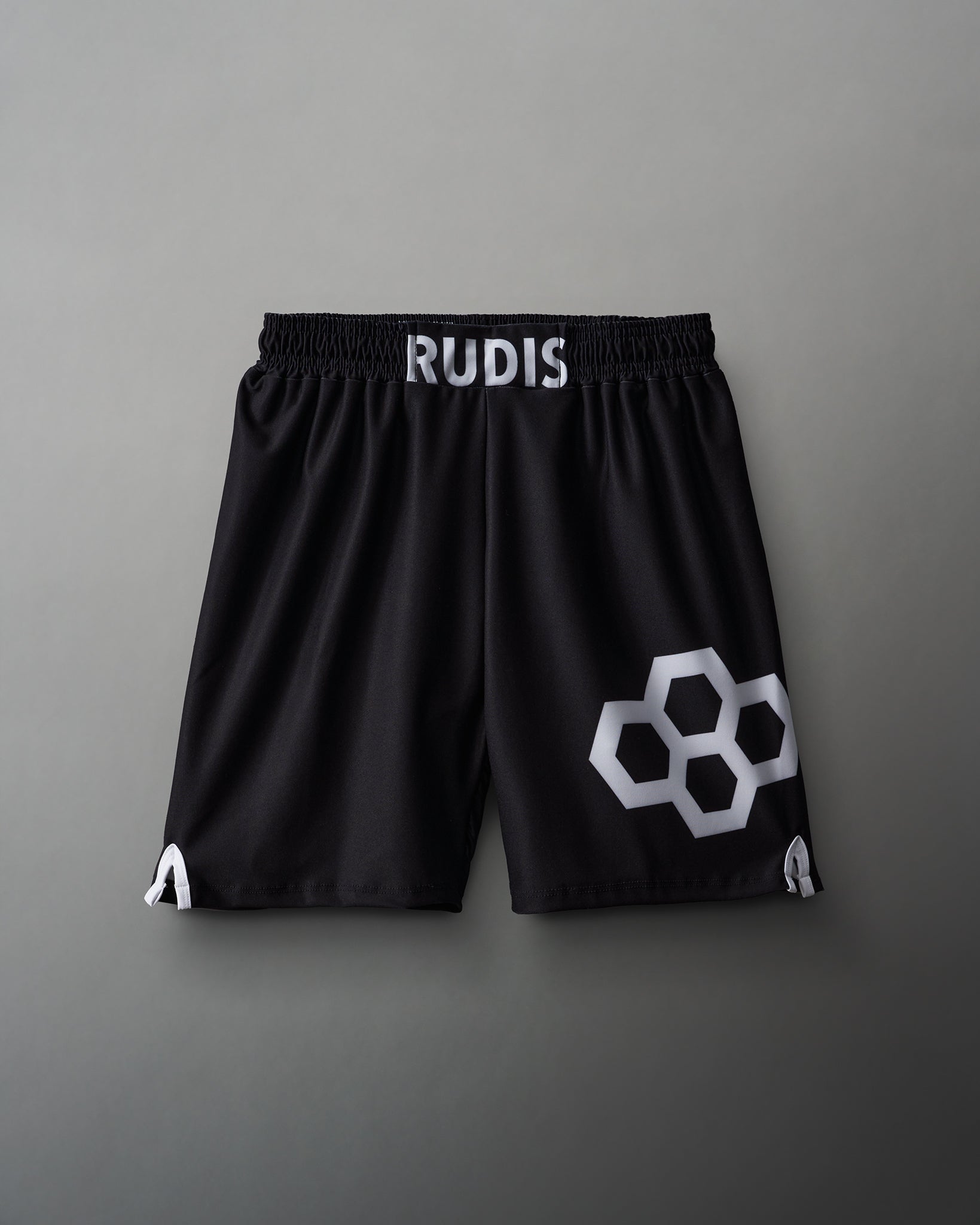 Black athletic shorts with a white 'RUDIS' logo on the waistband and a geometric honeycomb design on the lower left leg, made from lightweight fabric for sports.