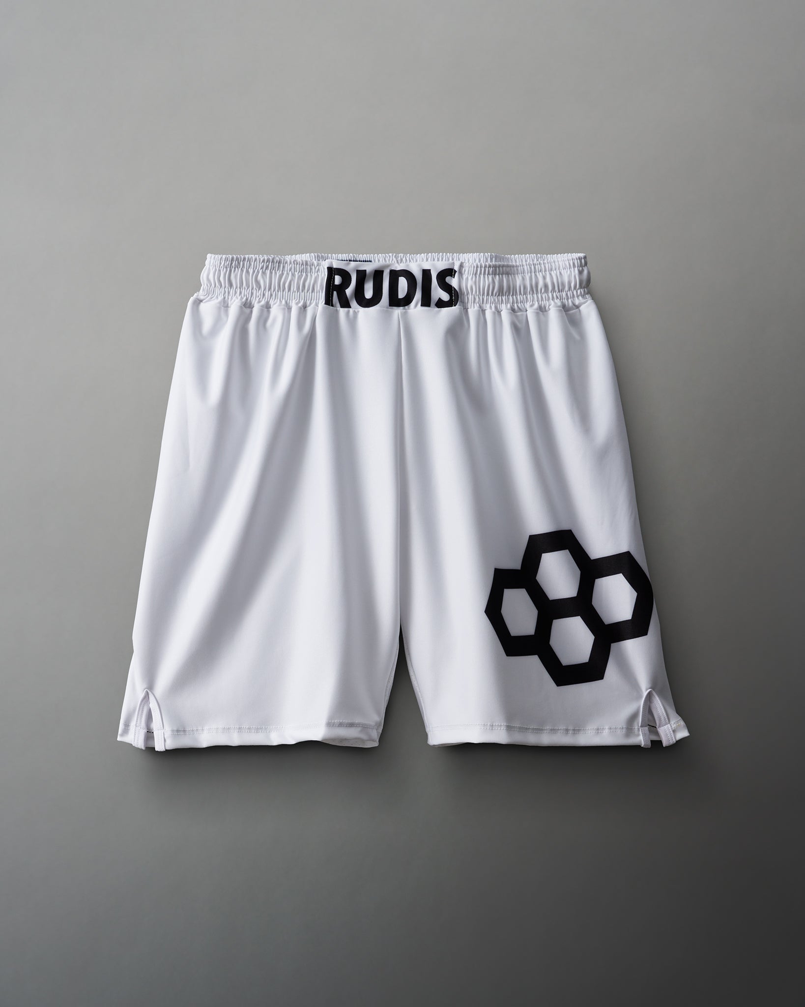 White athletic shorts with a black 'RUDIS' logo on the waistband and an interlocking hexagon graphic on the side, showcased against a gray background.