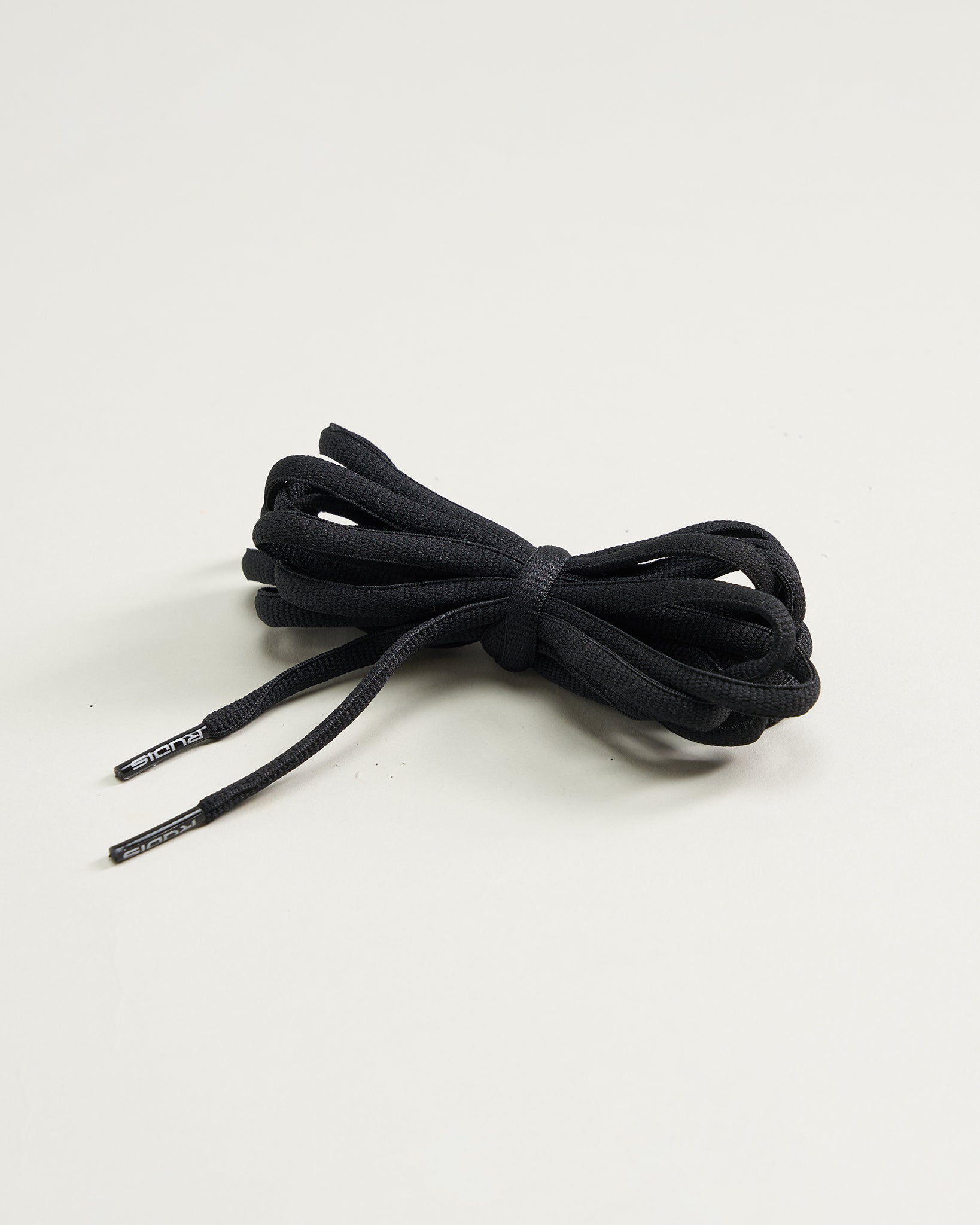 A neatly tied bundle of black shoelaces sits on a light green background showcasing their sleek design and ends with small metallic tips