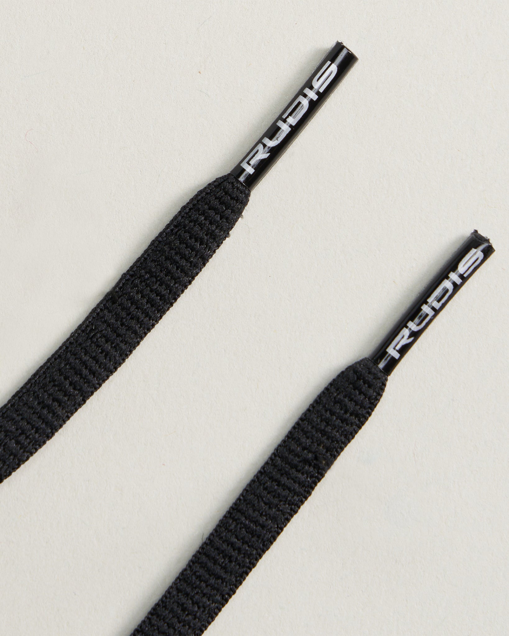 Close-up view of two black shoelaces placed on a light-colored surface featuring plastic ends with branding details