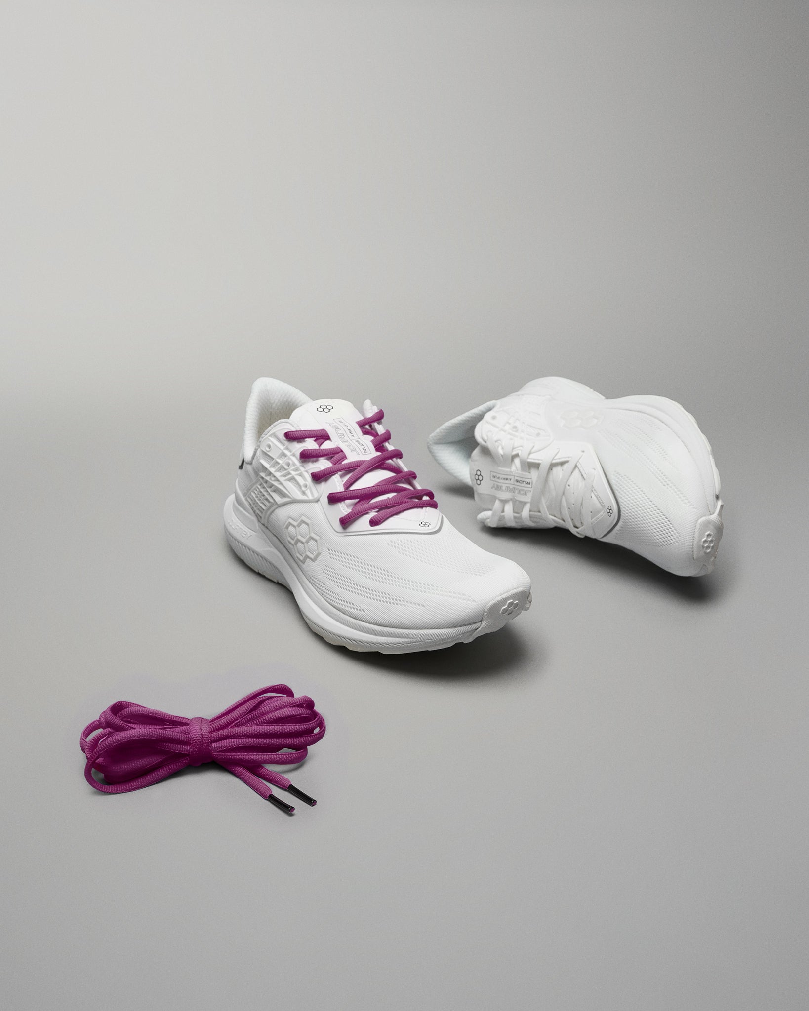 A pair of stylish white athletic shoes with purple laces alongside an extra set of purple shoelaces set against a neutral gray background