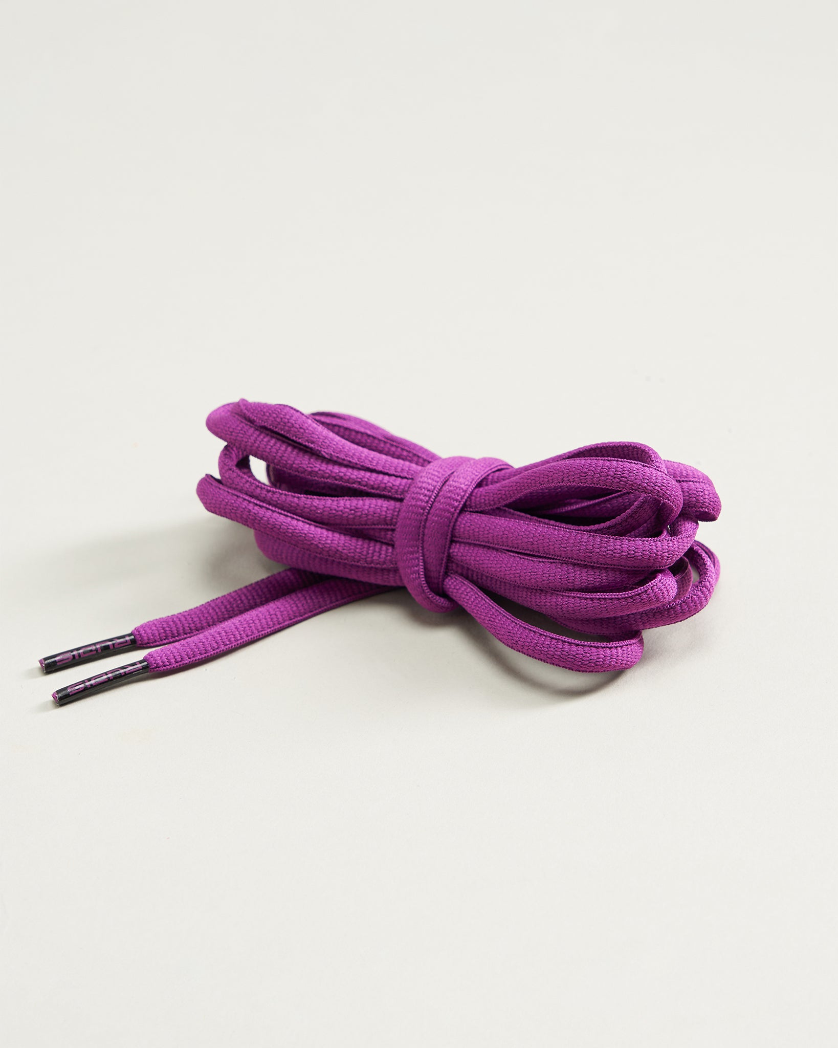 A bundle of vibrant purple shoelaces neatly coiled with aglets on both ends resting on a light background