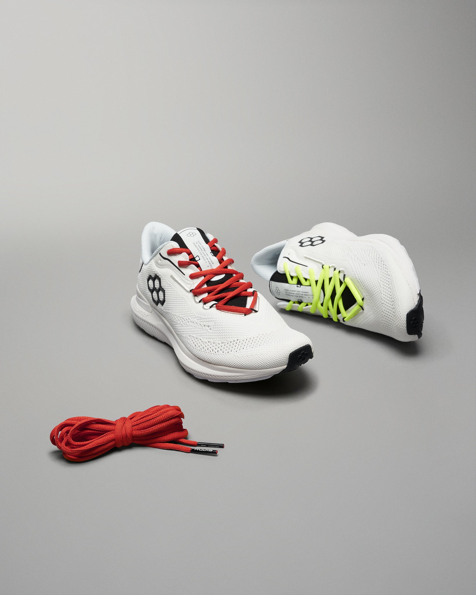 A pair of modern athletic shoes in white featuring red and neon green laces accompanied by a separate bundle of red shoelaces