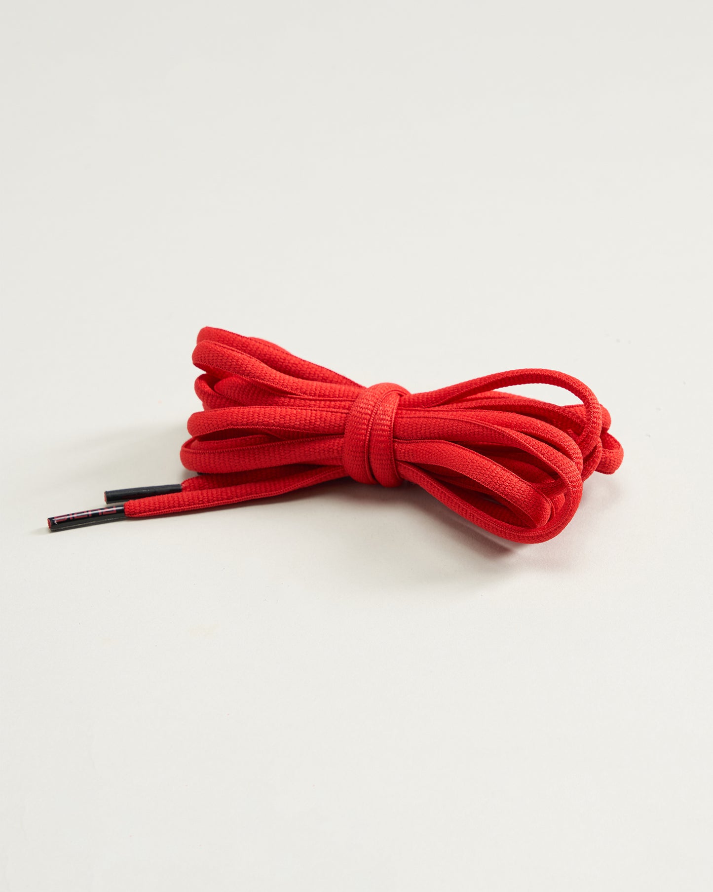 A vibrant red shoelace neatly tied in a bow resting against a light beige background