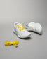 A pair of stylish white athletic shoes with yellow laces accompanied by an extra set of yellow laces on a neutral background