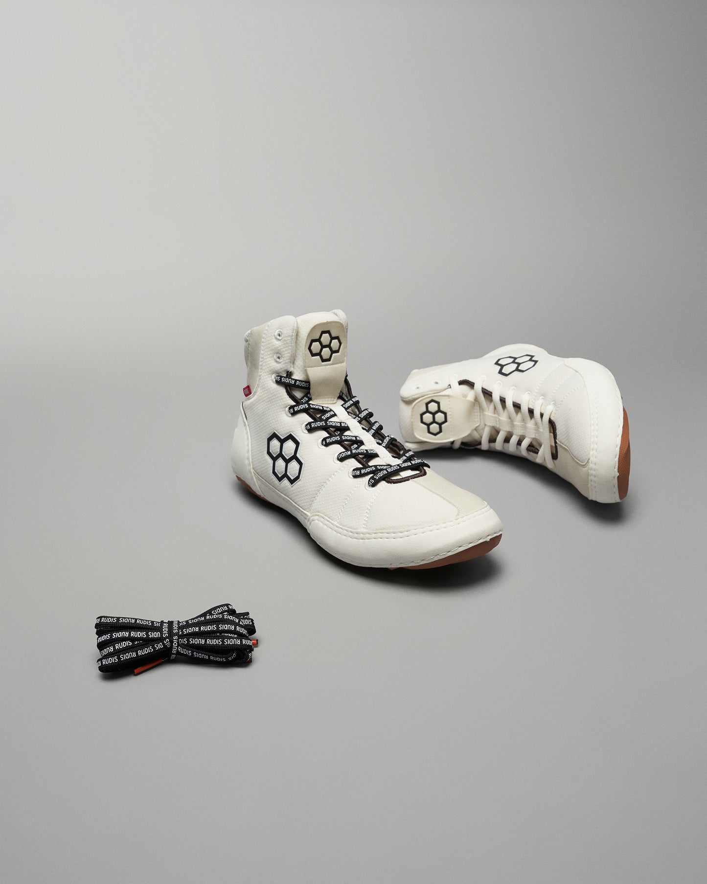 A pair of modern white high-top shoes with black accents and a pair of patterned black laces presented against a neutral background