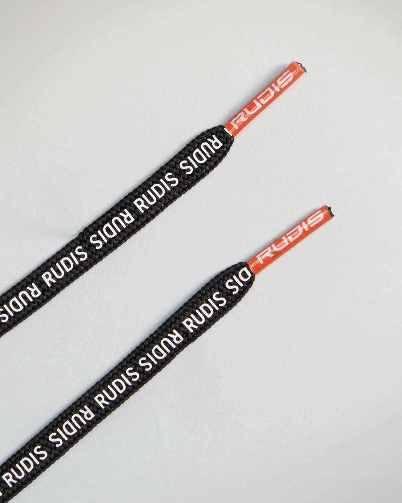 Black shoelaces with red tips featuring RUDIS branding laid against a light gray background