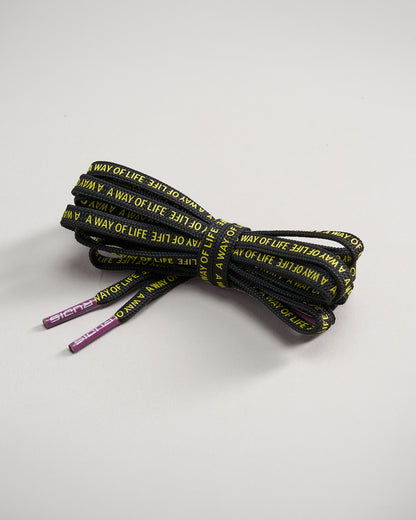 A tightly coiled pair of black shoelaces featuring repeating yellow text that says A WAY OF LIFE along with purple aglets at each end