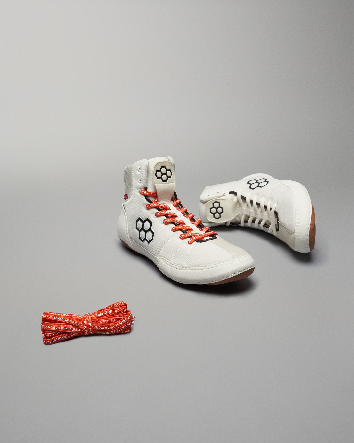 A pair of stylish white high-top shoes with orange laces and a distinctive logo accompanied by a second pair of laces in a matching color and design