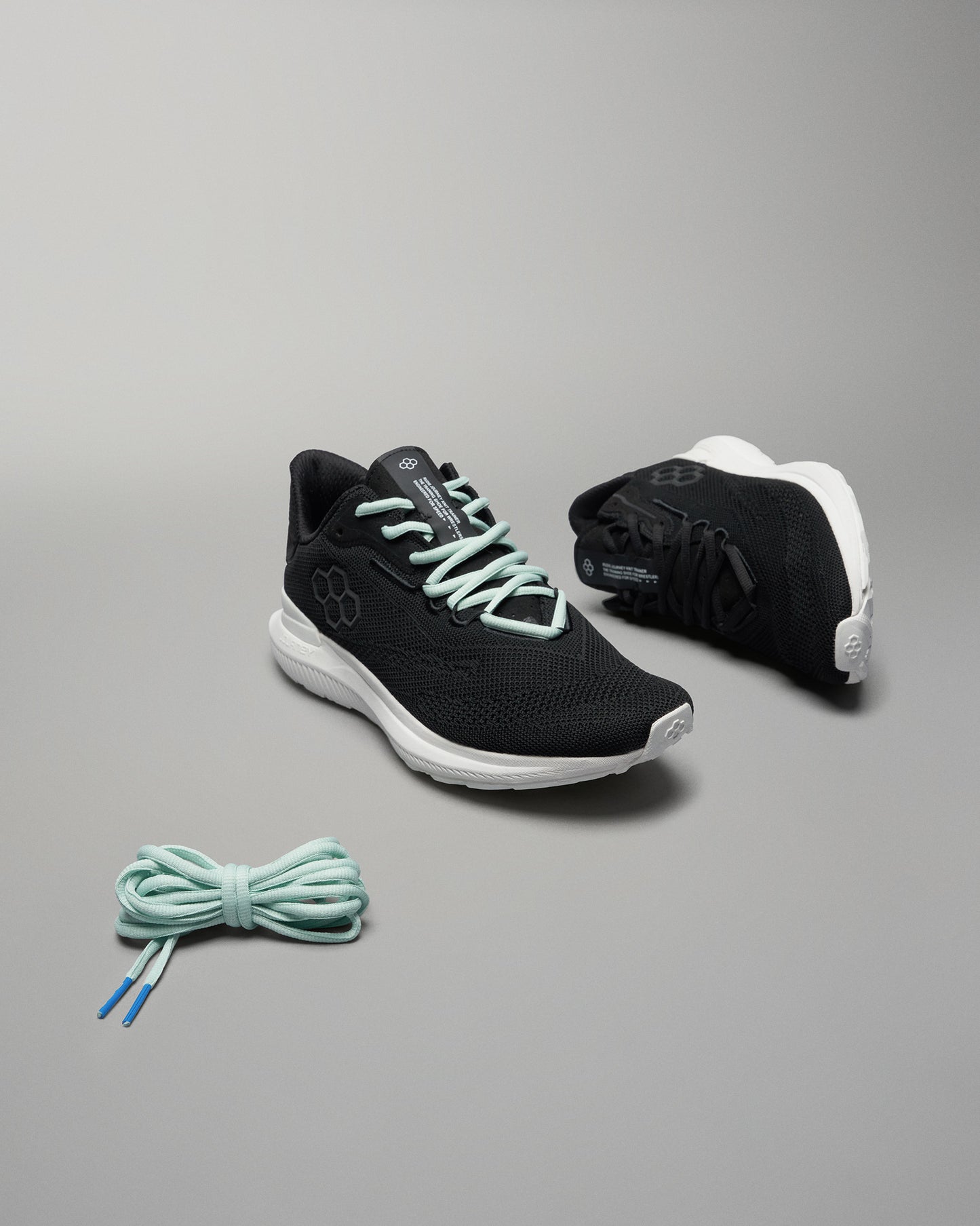 This image features a pair of black athletic shoes with turquoise laces and a light-colored sole accompanied by a matching pair of laces positioned beneath them