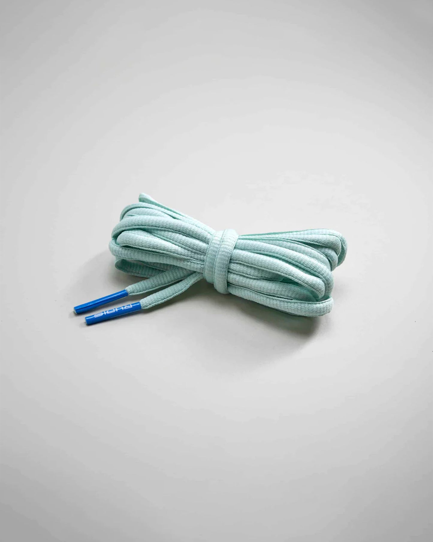 A neatly tied pair of mint green shoelaces with blue aglets on a light gray background