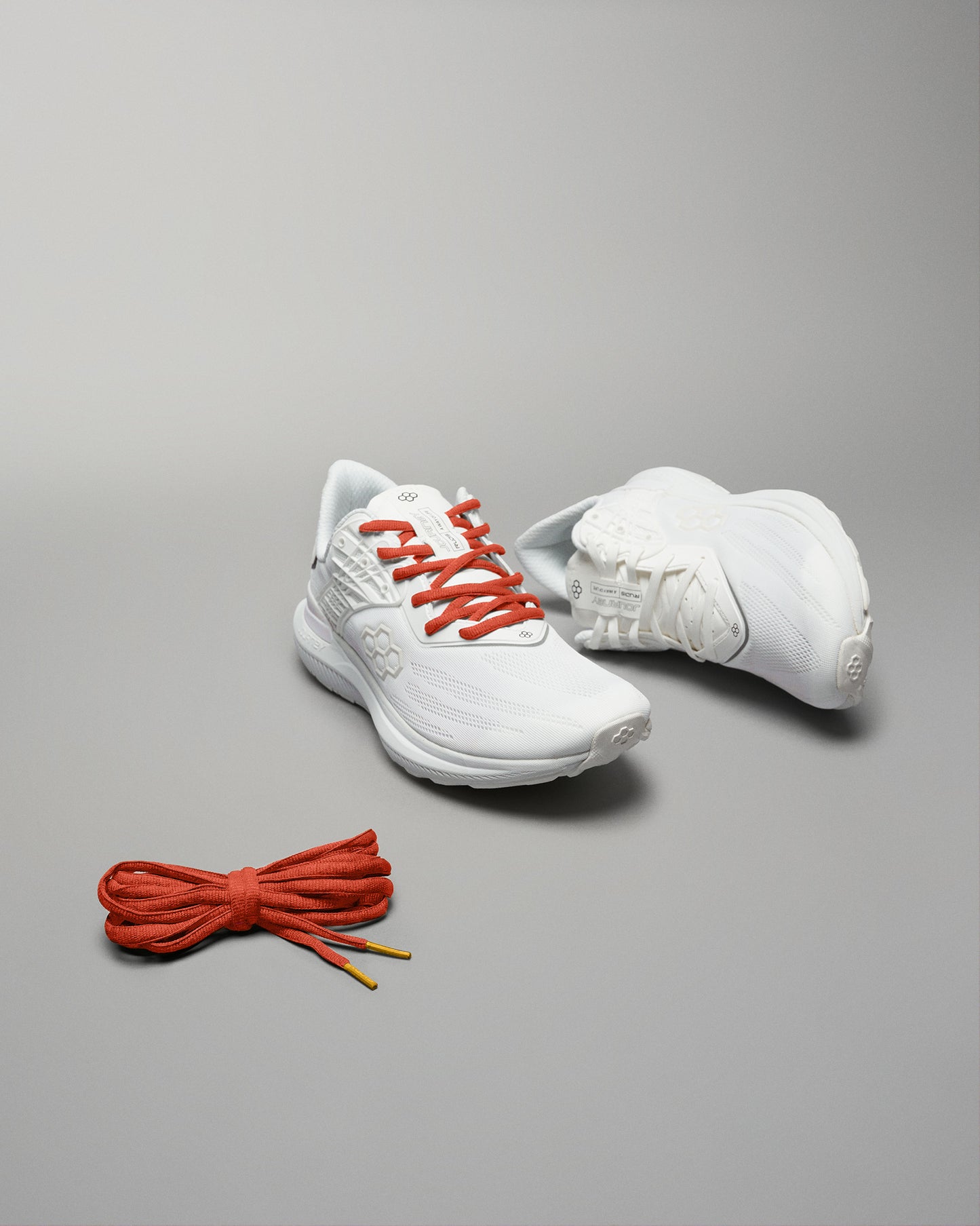 A pair of modern white athletic shoes with red laces displayed alongside a bundle of matching red shoelaces on a minimalist background