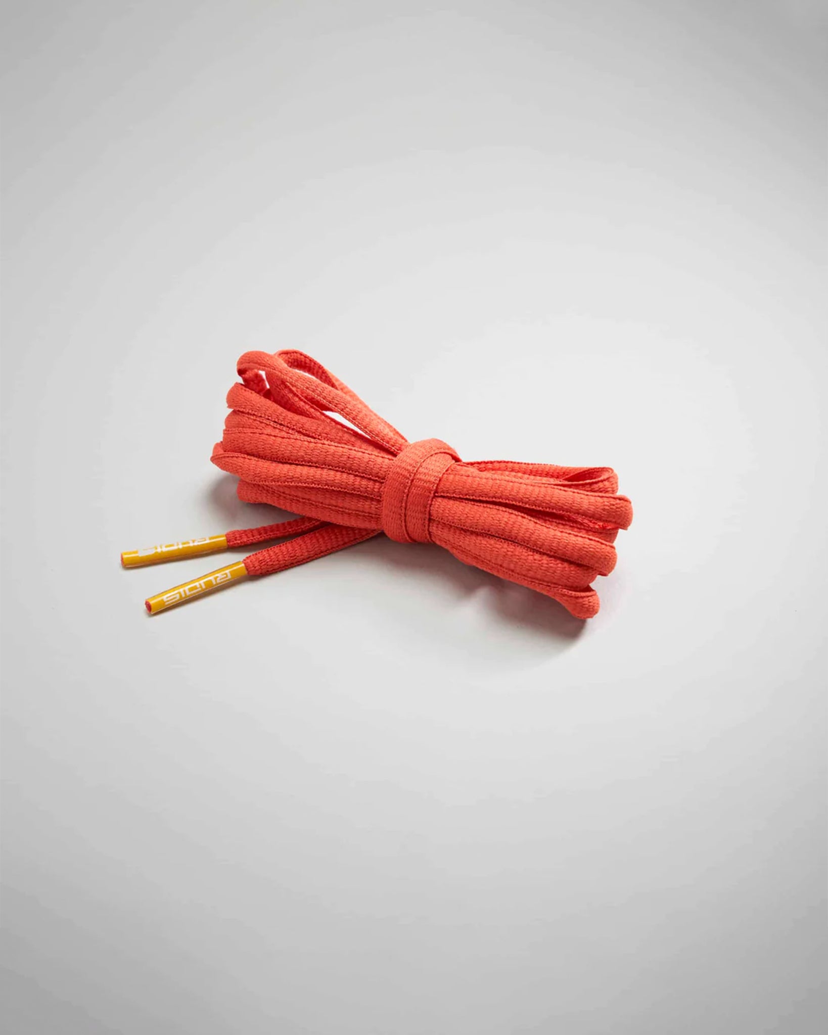 A bundle of vibrant orange shoelaces with yellow-tipped ends elegantly arranged on a light gray surface