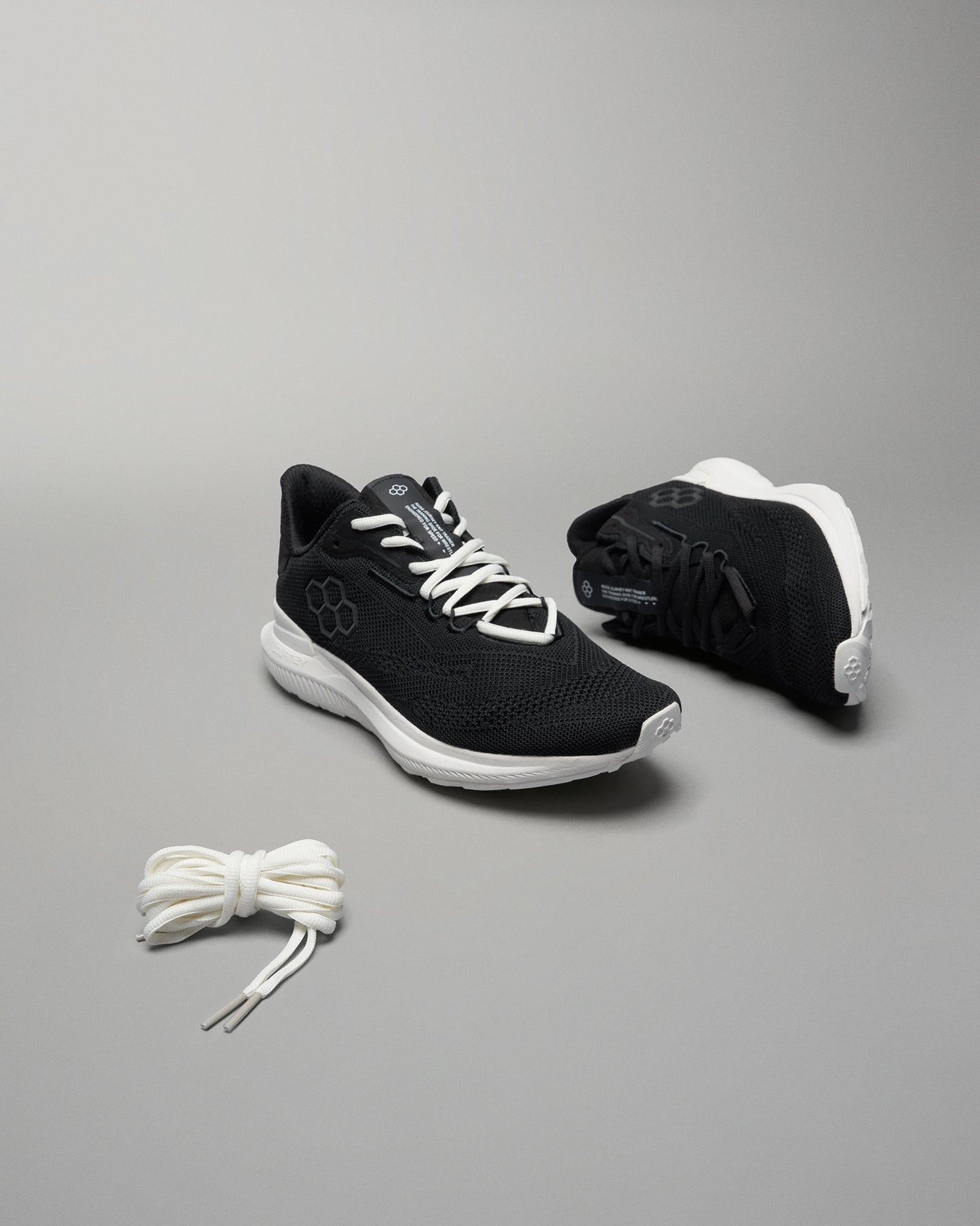 A pair of black athletic shoes with a breathable mesh upper and white accents paired with a neatly tied set of white shoelaces on a gray background