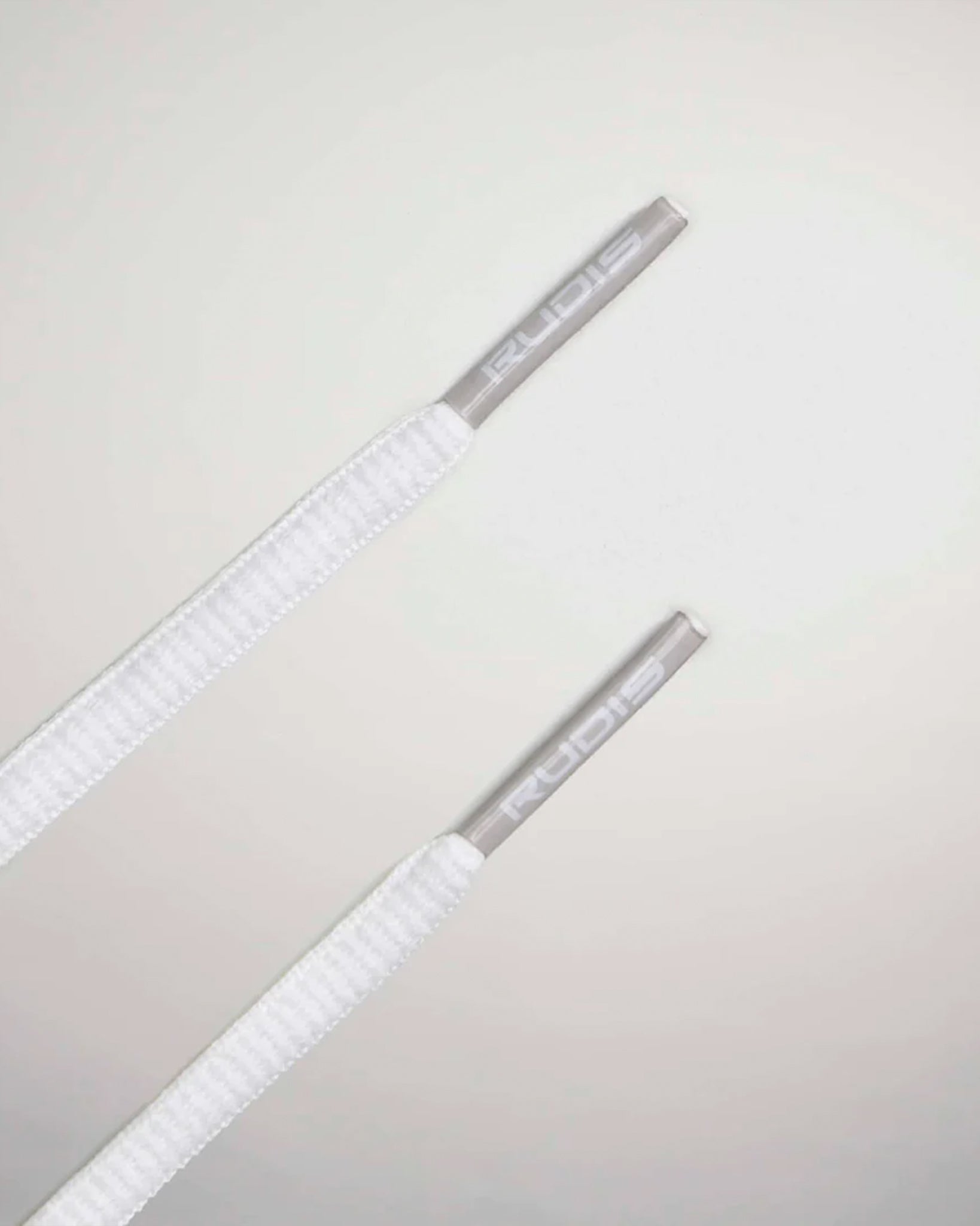 This close-up image features two white shoelaces with textured fabric and silver aglets inscribed with RUDIS