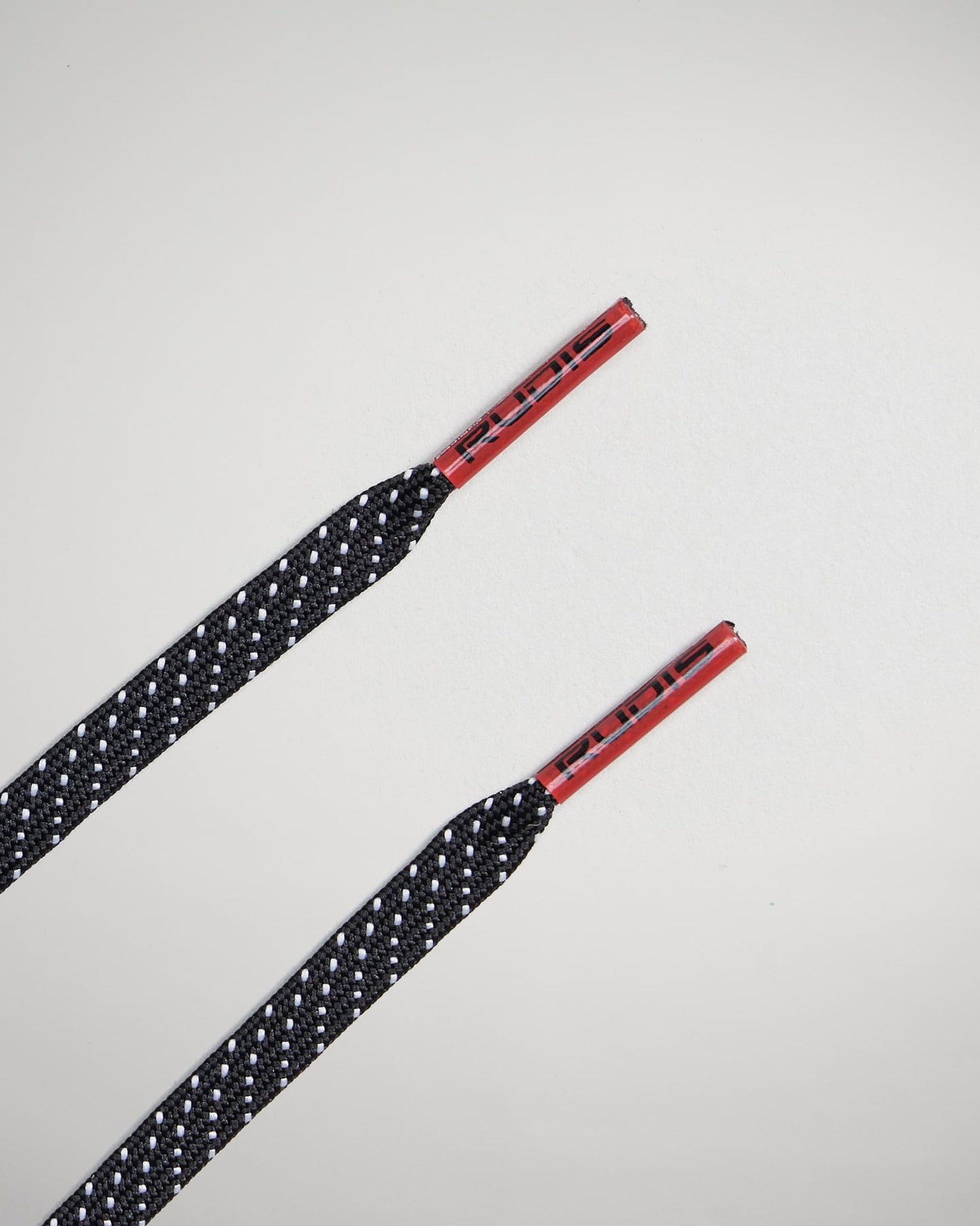 A close-up view of black shoelaces featuring red aglets designed with a textured pattern and reflective accents for visibility and style