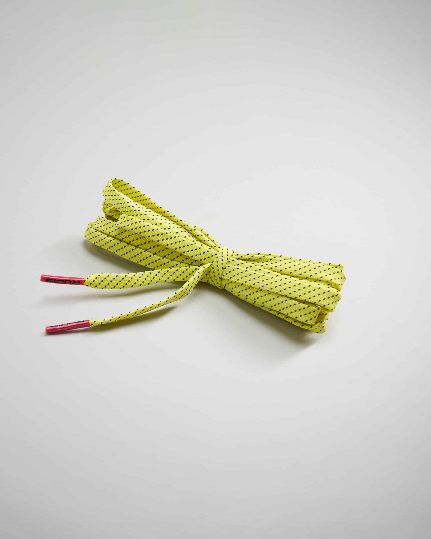 A bundle of vibrant yellow shoelaces with black dots tied together neatly on a light gray surface