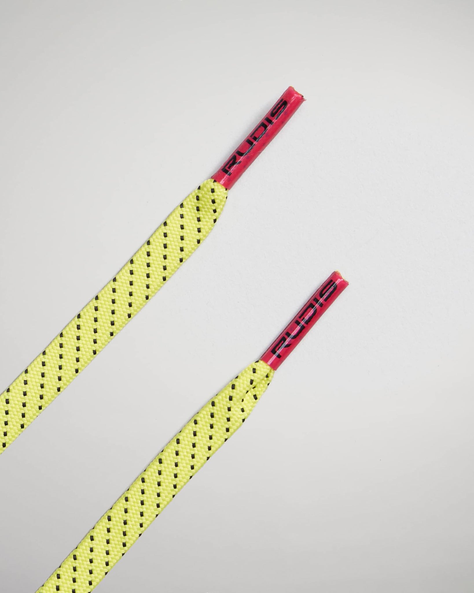 A vibrant yellow shoe lace with black perforations and red aglets featuring the brand RUDIS