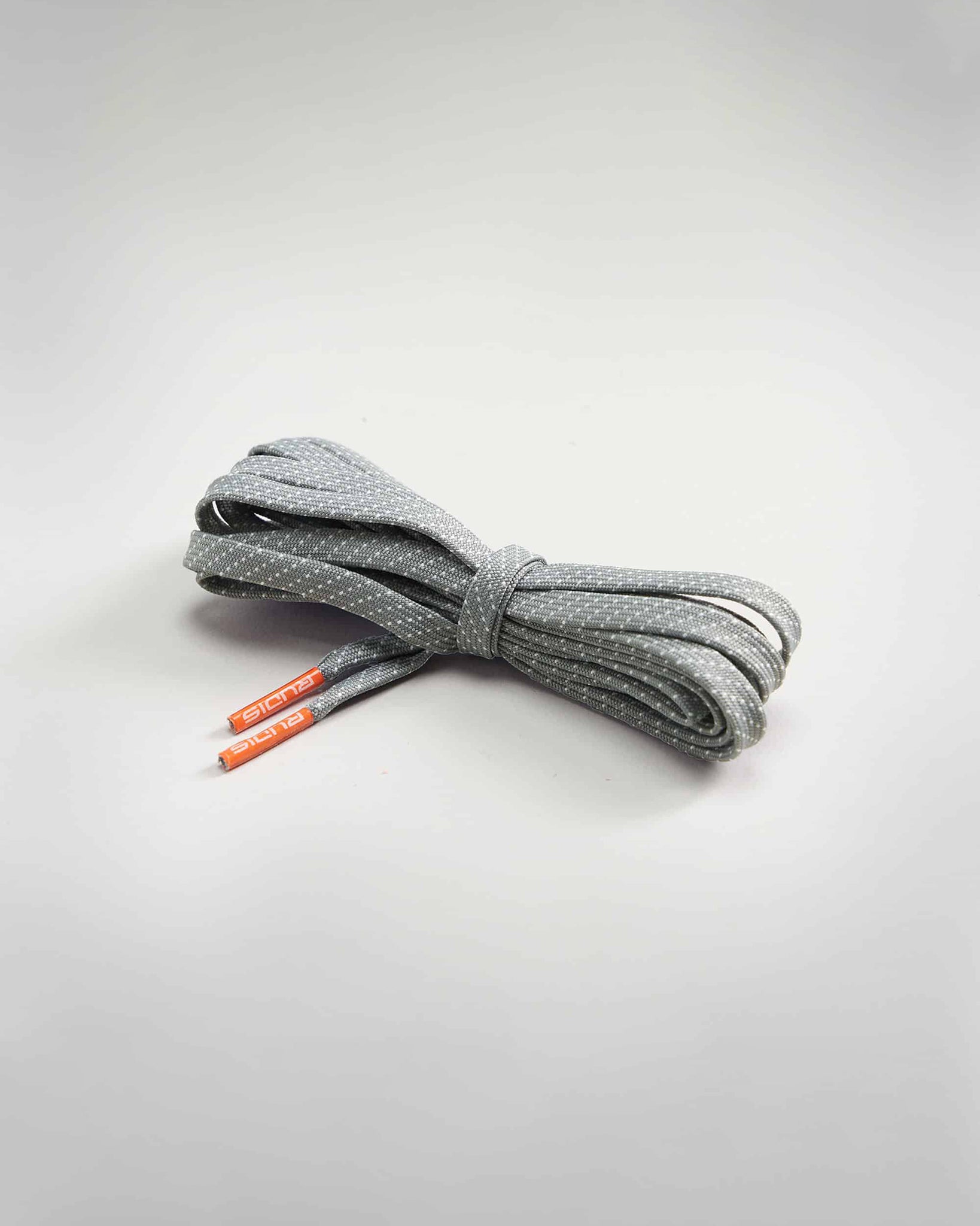 A neatly rolled pair of gray shoelaces featuring a dotted pattern and orange tips resting on a light gray background