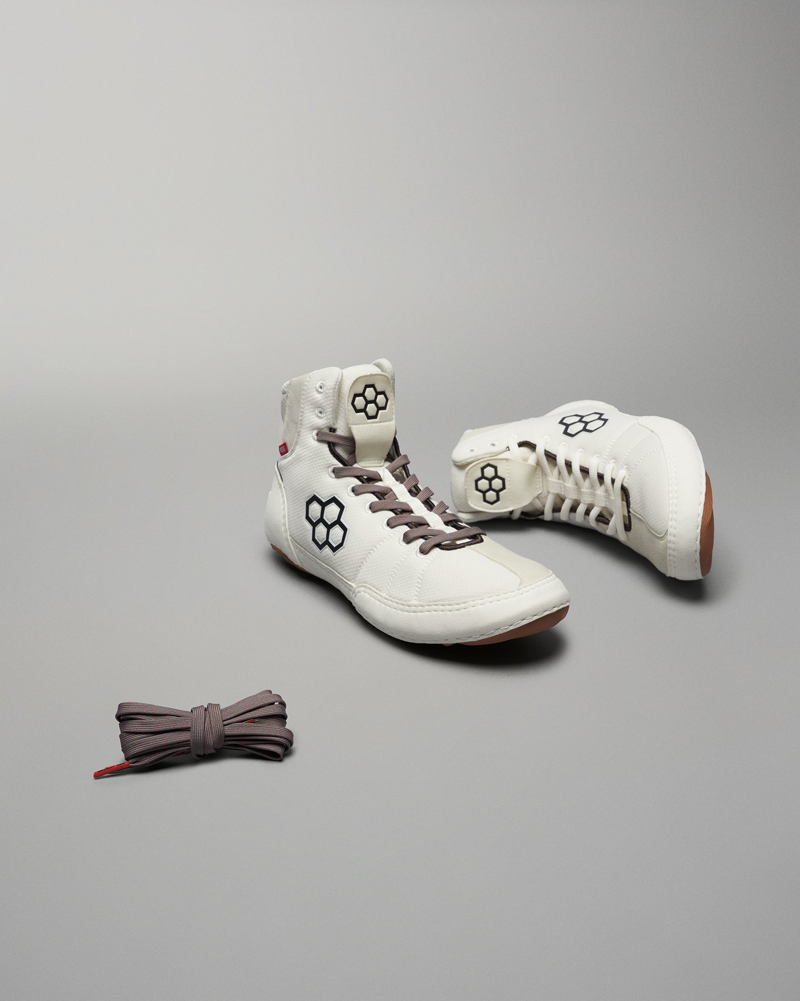 A pair of stylish white sneakers with a unique hexagonal design accompanied by matching brown laces set against a minimalist gray background