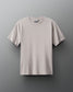 A light beige T-shirt with a round neckline and short sleeves is displayed against a muted gray background, showcasing a comfortable texture and subtle branding.