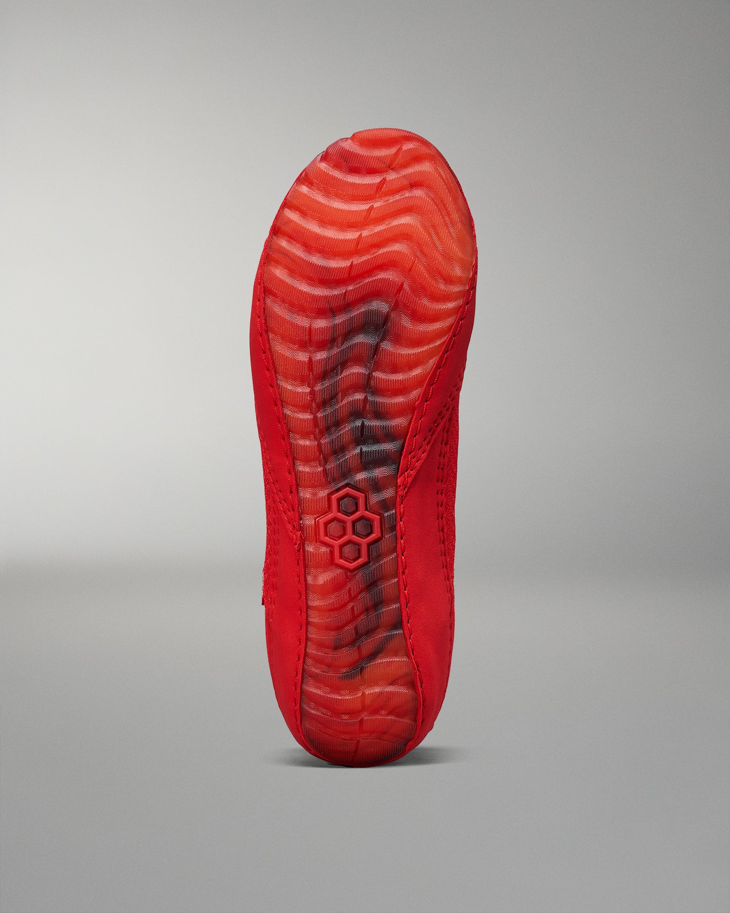 The underside of a bright red shoe displays a textured sole with intricate patterns for grip against a soft gray background.