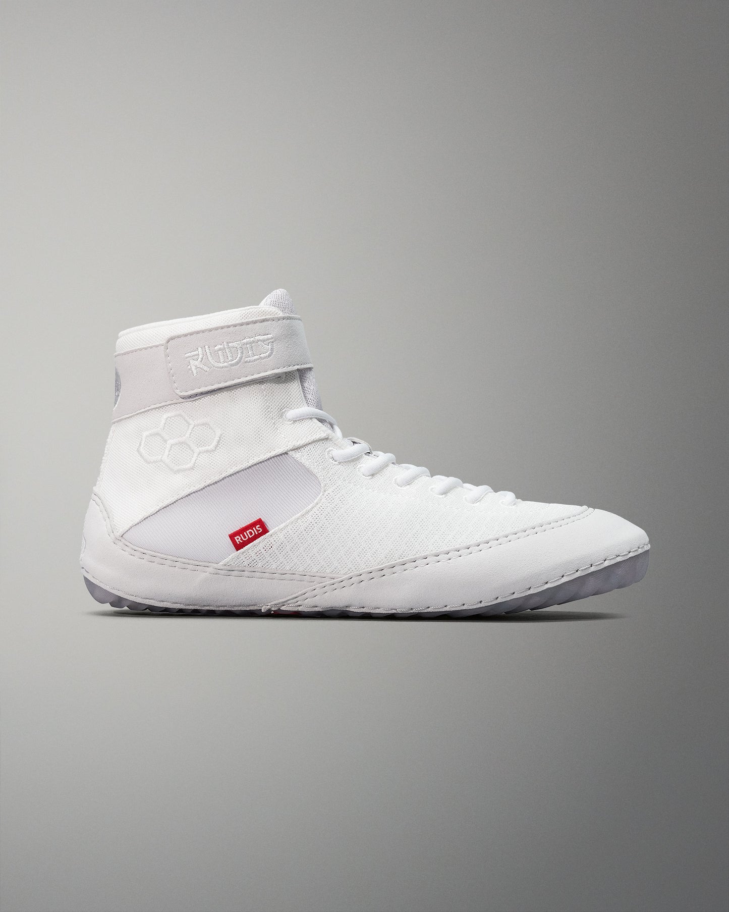 High-top white wrestling shoes with a textured fabric finish and red branding feature a smooth sole designed for traction, set against a muted gray background.