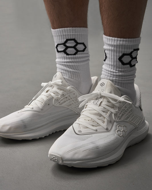 A pair of stylish white athletic shoes worn with textured white socks featuring a black hexagonal pattern set against a minimalist background