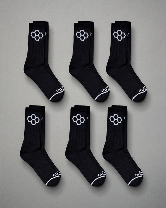 A display of six pairs of black athletic socks featuring a distinctive white hexagonal logo and stylish design details laid out on a gray background