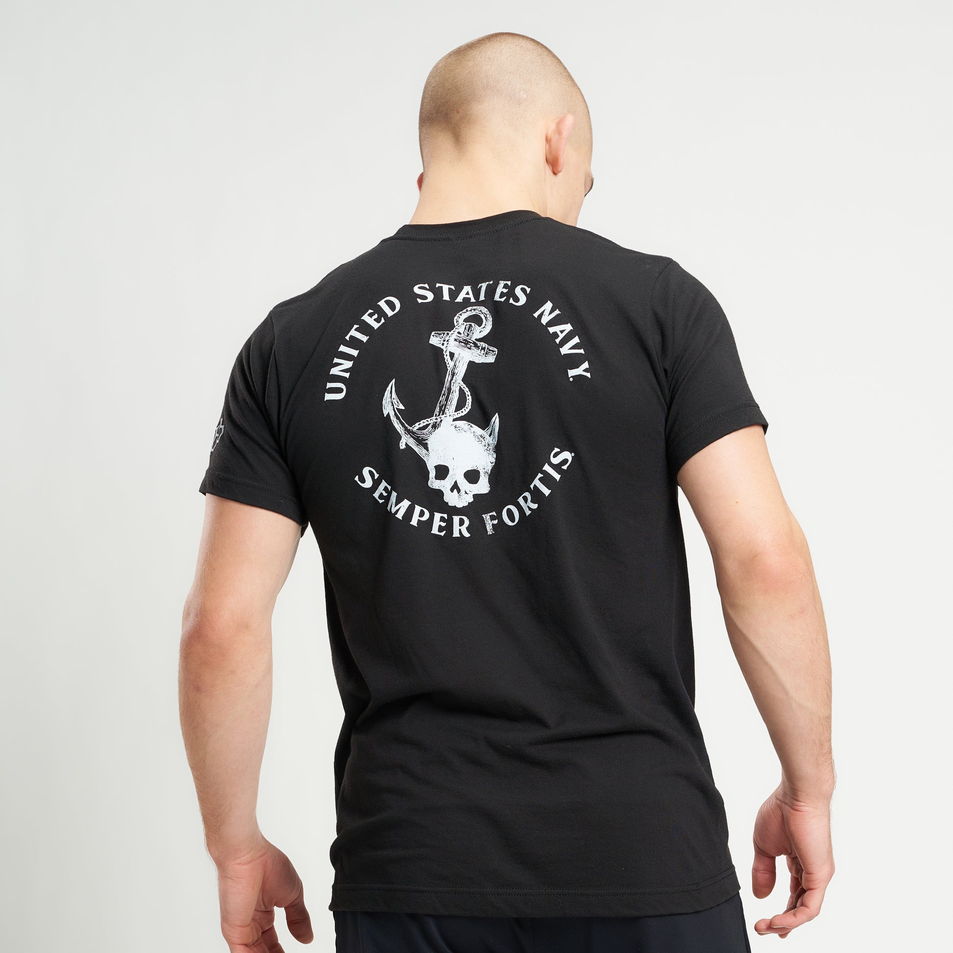 A man wearing a black t-shirt with a United States Navy design featuring an anchor and a skull standing with his back to the viewer