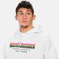 A young man wearing a white hoodie with colorful Sports Illustrated branding looking thoughtfully to the side against a neutral background