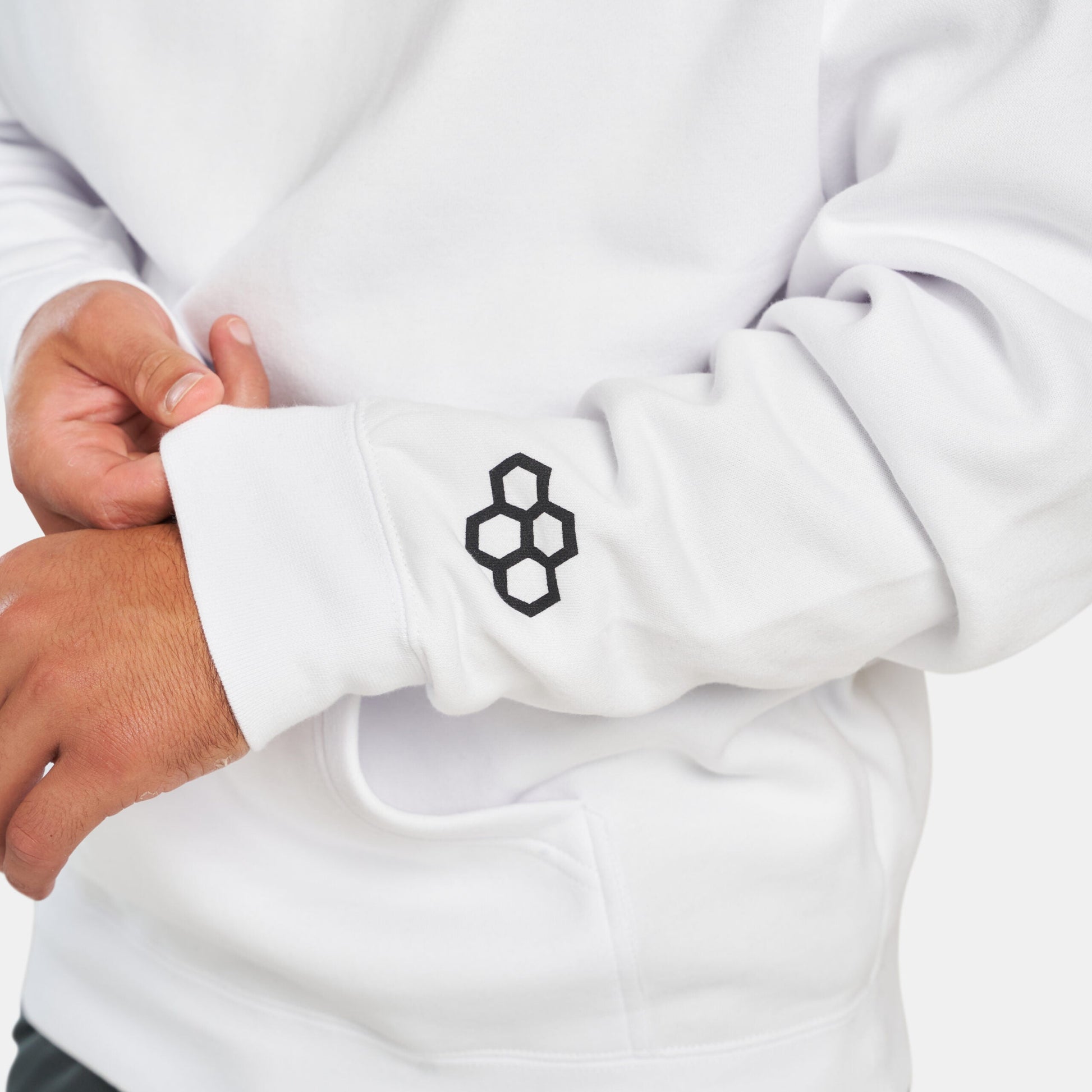 A close-up of a person wearing a white sweatshirt with a black geometric logo on the sleeve highlighting the garments design and material